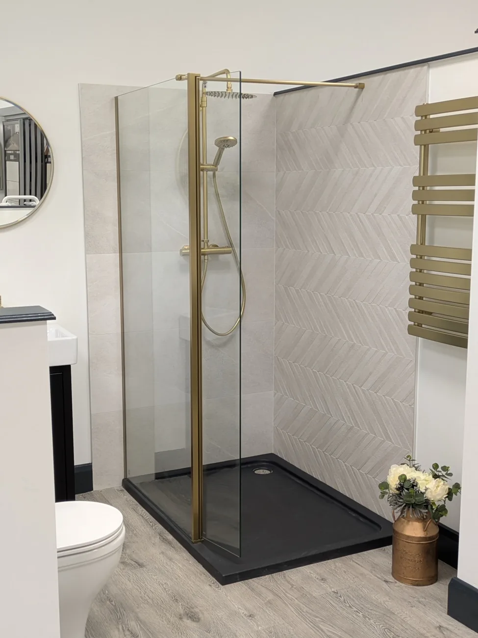 Walk-in shower with brushed gold fittings, chevron feature tiles and black stone shower tray